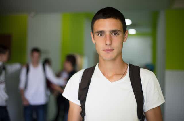 Teenage boy at school, wearing backpack, with other students in background 