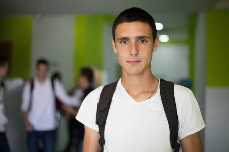 Teenage boy at school, wearing backpack, with other students in background