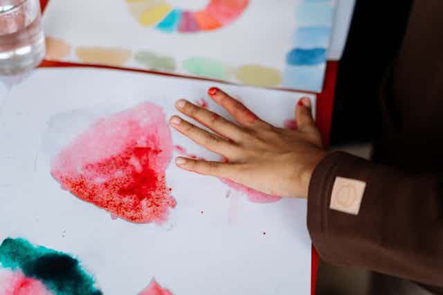 Child paints with watercolours and their hand