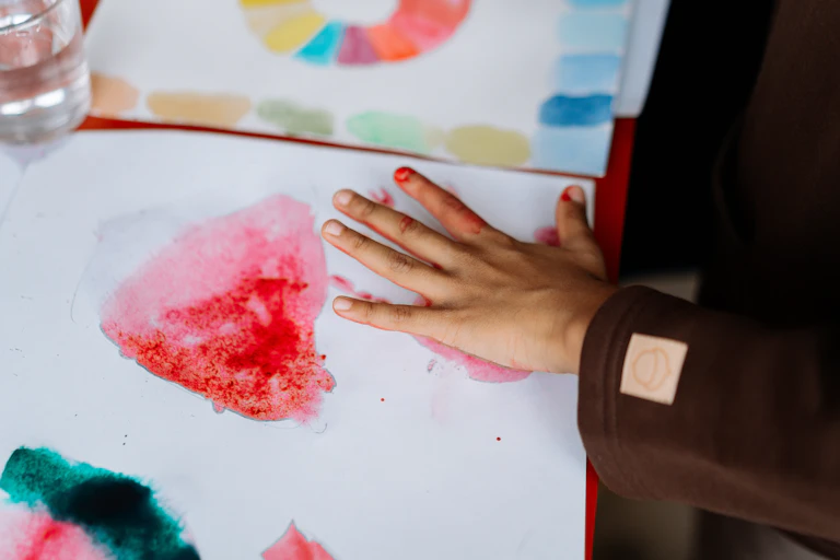 Child paints with watercolours and their hand