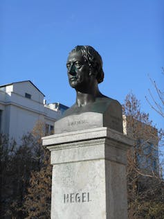 A black bust of Hegel's head sits atop a grey concrete column emblazoned with the word 'Hegel'