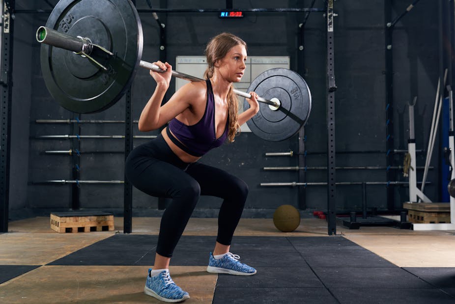 A woman performs a barbell squat in the gym.