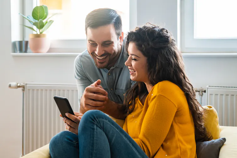 A couple smile while looking at something on a smartphone.