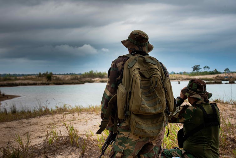 Two rangers look out over a lake in a sandy plain.