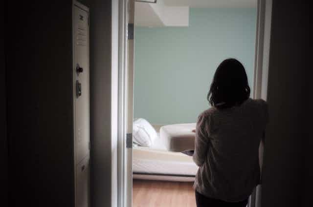A woman is seen from behind standing in the doorway of a bedroom holding bedding.