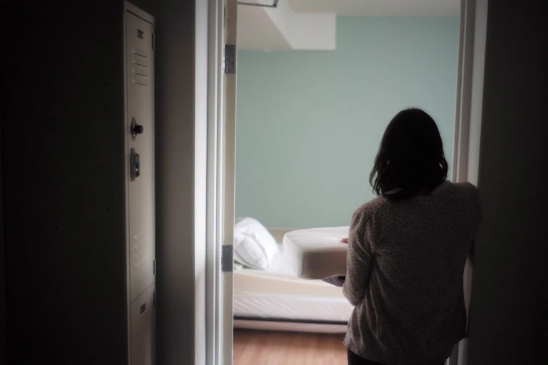 A woman is seen from behind standing in the doorway of a bedroom holding bedding.