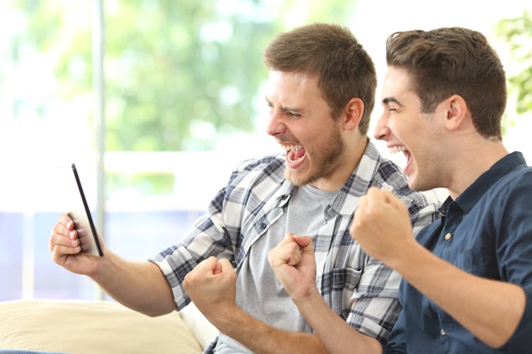 Two young white men holding a phone and cheering.