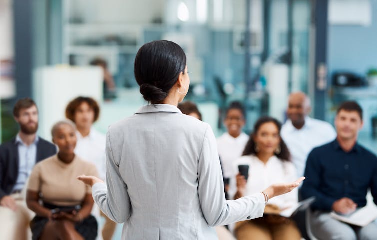 A well-coiffed woman teaches a roomful of professionals.