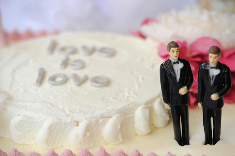 Two male figurines in formal suits stand on a white cake that says love is love