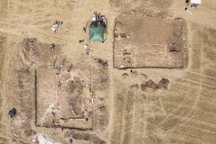 An aerial view of the excavation shows the outline of the former buildings in a parched, brown field.