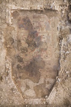 The fully exposed Trojan War mosaic within the outline of the dining room. Guests would have sat in the apse at the bottom of the photograph, while the villa owner narrated the story, which is illustrated over three successive panels