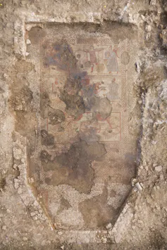 The fully exposed Trojan War mosaic within the outline of the dining room. Guests would have sat in the apse at the bottom of the photograph, while the villa owner narrated the story, which is illustrated over three successive panels