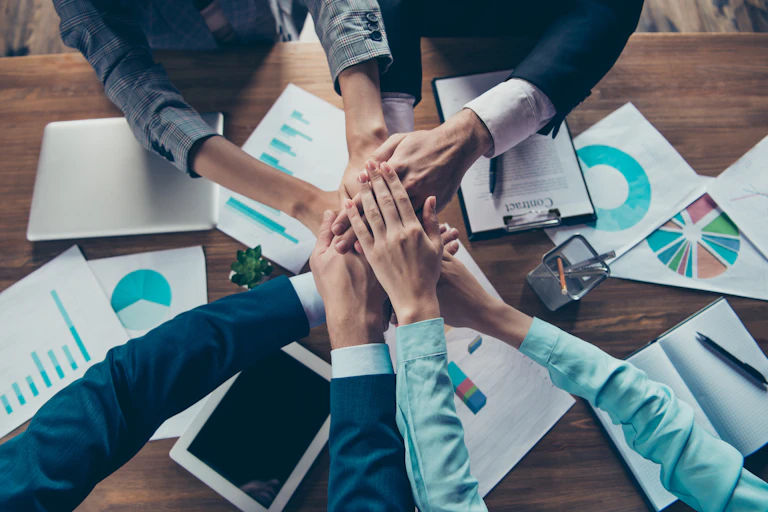 A group of people putting their hands together in the middle of a table covered with paperwork