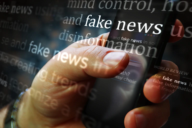 A person's hand is on a mobile phone in an illustration with the words "fake news" and "disinformation" overlayed.