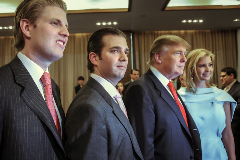 Three white man wearing suits and a white woman wearing a blue dress stand in a row posing