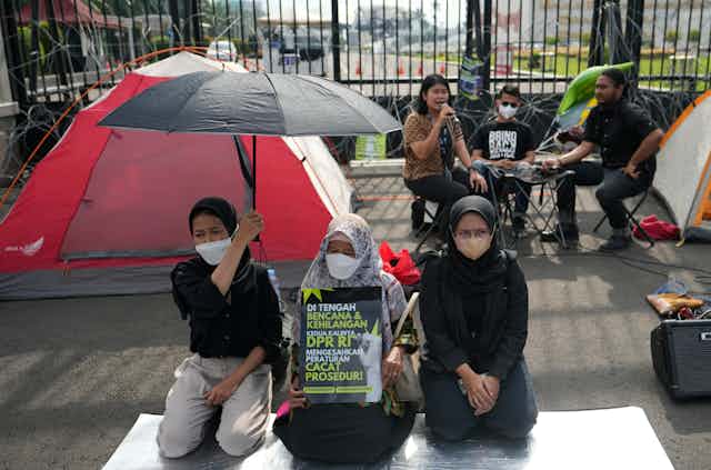 Activists protest in front of the parliament building in Jakarta, Indonesia, Tuesday, Dec. 6, 2022. Indonesia's Parliament passed a long-awaited and controversial revision of its penal code Tuesday that criminalizes extramarital sex for citizens and visiting foreigners alike.