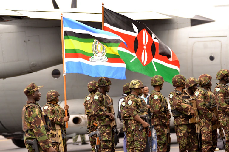 Men in military uniform and carrying guns stand beside a plane.