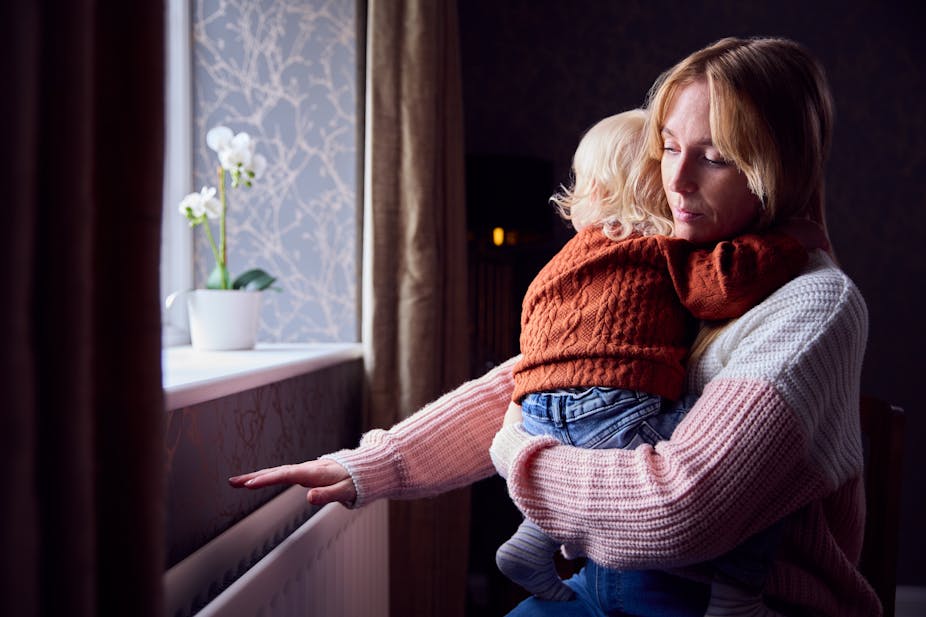 A mother holding her child with her hand outstretched over a radiator.
