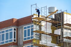 A man standing at the top of scaffolding installing insulation to the external wall of a building.