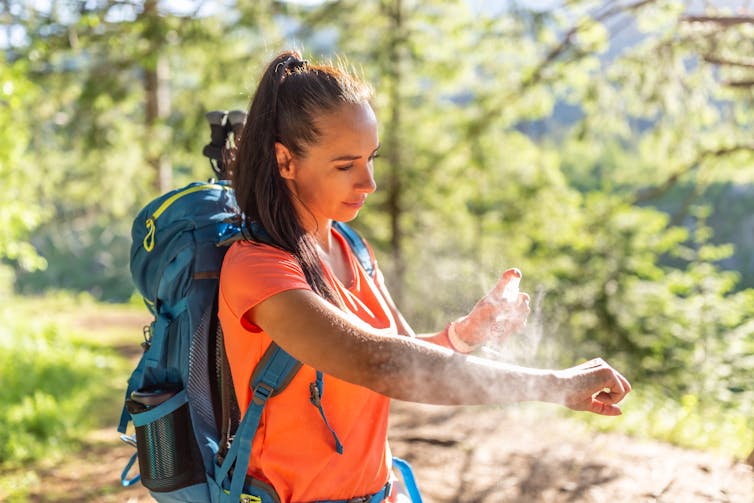 woman with backpack in woods sprays her arm