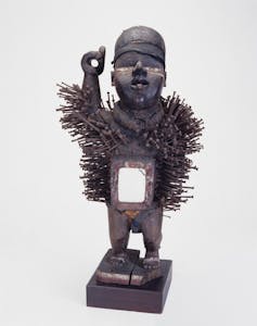 Nail-studded container for nkisi force, carved wooden figure with mirrored container, Bakongo people, west-central Africa, 1882-1920. Front three quarter view. White background