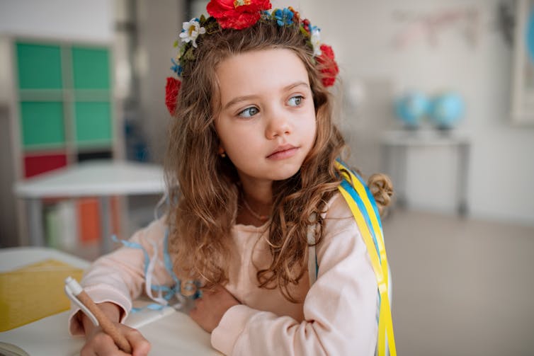 A young girl sits at her desk at school, while staring out the window daydreaming.