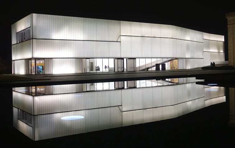 A white rectangular building seen reflected into water beside it.