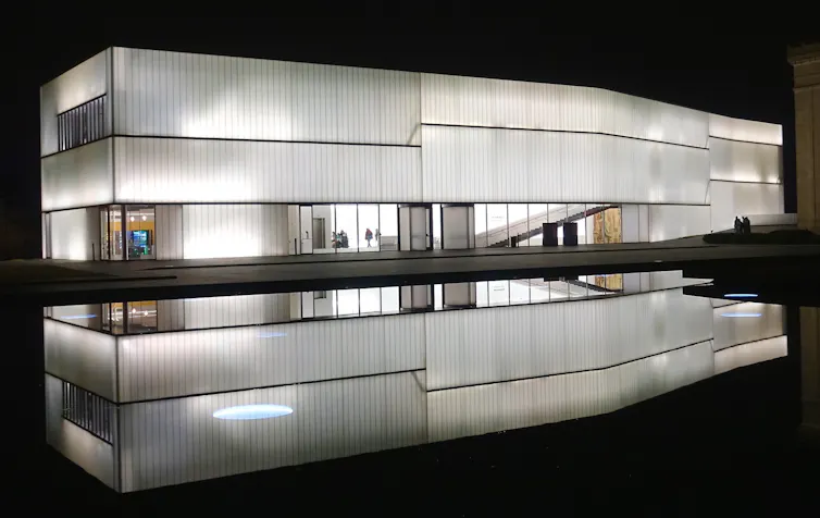 A white rectangular building seen reflected into water beside it.