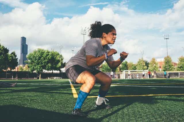 Une jeune femme à l’entraînement sur un terrain de football fait des squats.