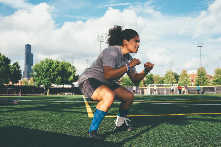 Une jeune femme à l’entraînement sur un terrain de football fait des squats.