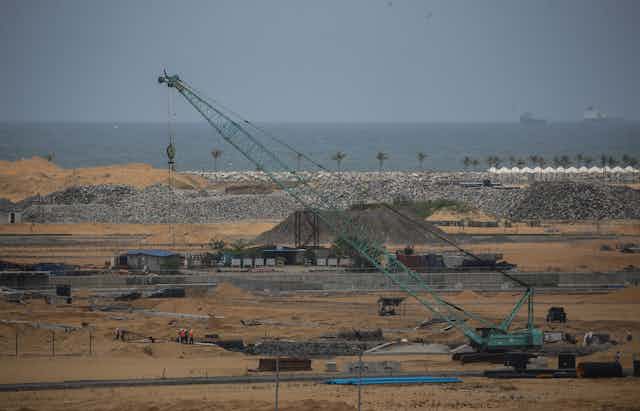 A crane and piles of rock and sand with the ocean in the background