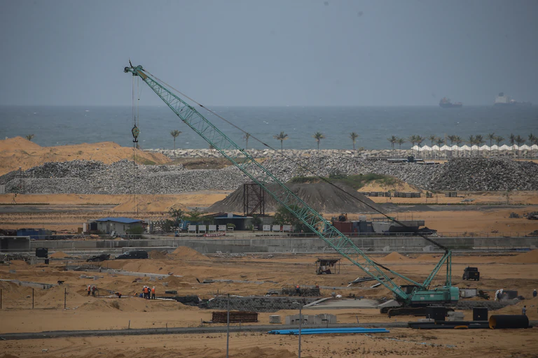 A crane and piles of rock and sand with the ocean in the background