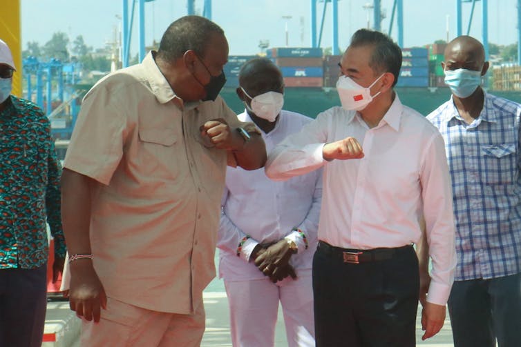 Two men wearing masks bump elbows on a pier