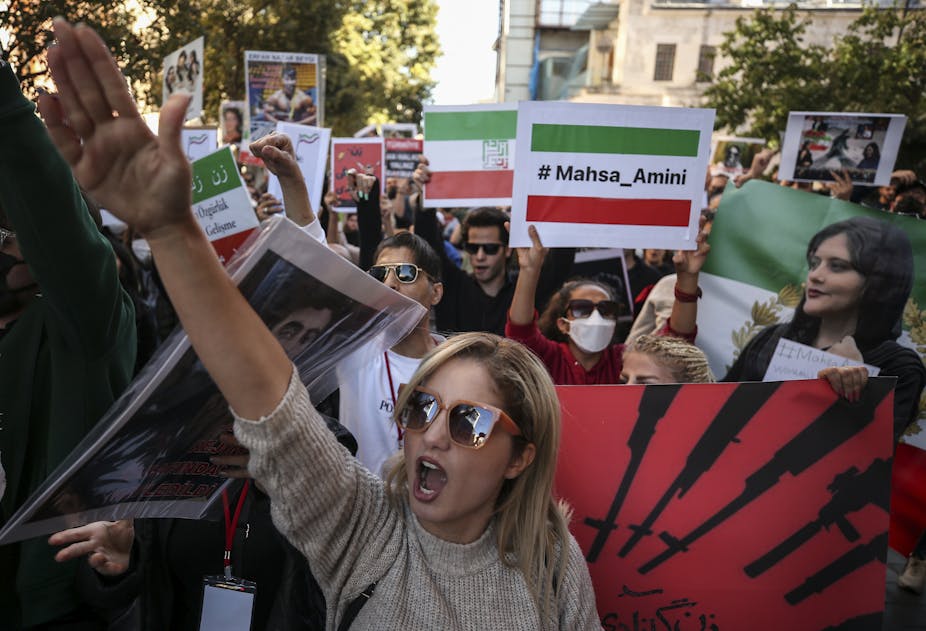 Iranian women carrying placards showing photo and name of Mahsa Amini while shouting slogans.