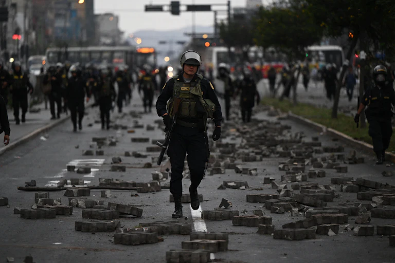 A heavily armed member of the police walks down a street with what looks like rubbled around him.