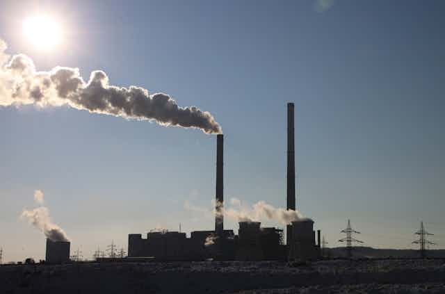 Silhouetted view of factory with smoke coming from chimneys