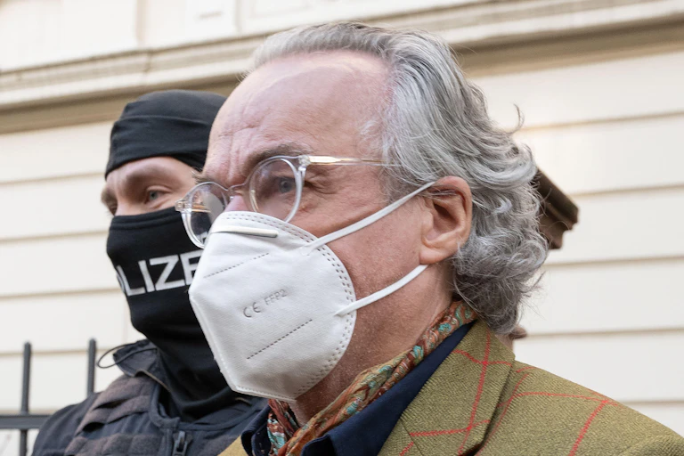 Heinrich XIII Prince Reuss wearing a face mask with a masked police officer behind him.