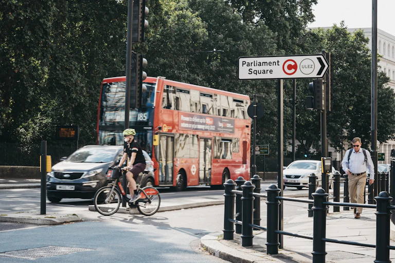 A bus with cars and cyclists, and pedestrians on a city street.