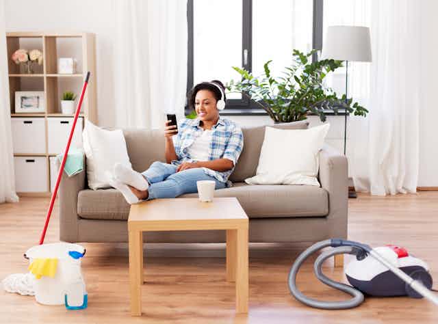 Image of a woman listening to music rather than cleaning, with hoover next to her.