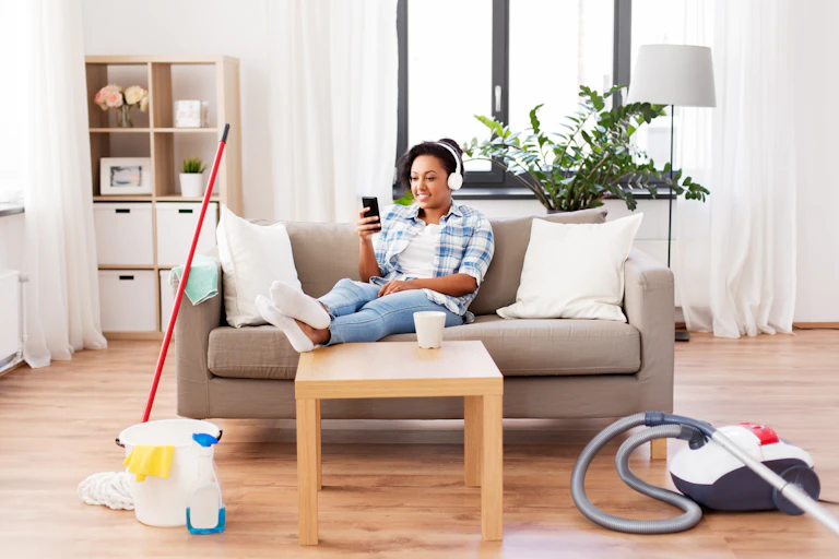 Image of a woman listening to music rather than cleaning, with hoover next to her.