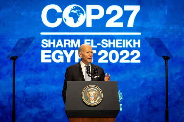 A man standing at a podium with a blue and white COP27 sign behind him.