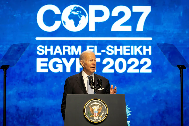 A man standing at a podium with a blue and white COP27 sign behind him.