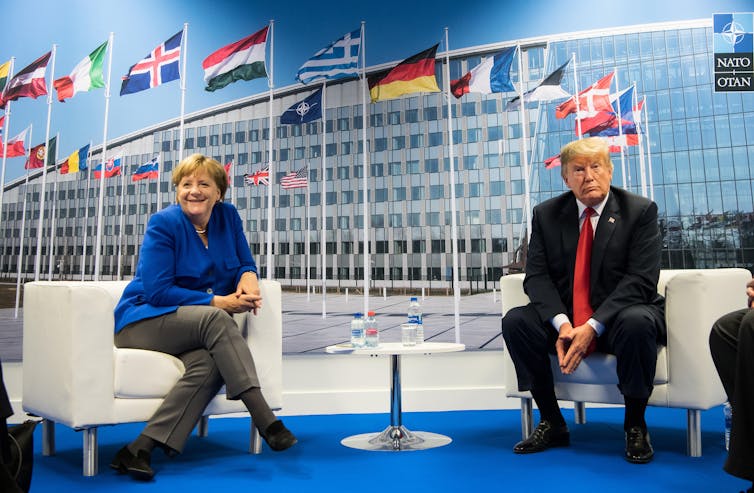 A woman and a man sitting on a sofa with flags behind them.