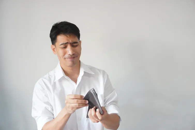 Image of a man looking at his empty wallet, unhappy.