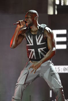 Stormzy performs holding a microphone and wearing a stab vest emblazoned with the Union Jack flag.