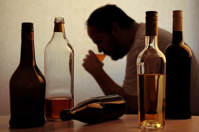 Silhouette of a man drinking alcohol with half drunk bottles in the foreground