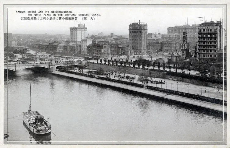 A black and white photograph of a river with boats and bridges.