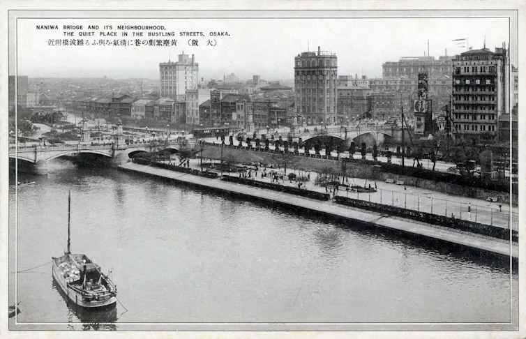 A black and white photograph of a river with boats and bridges.