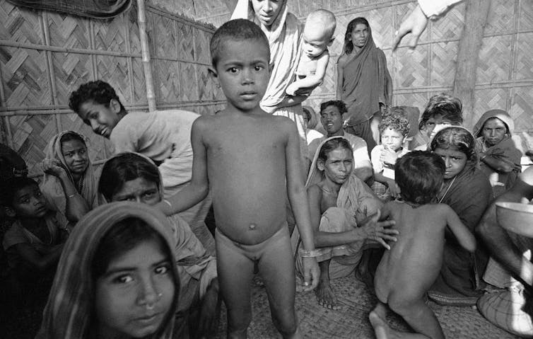 Women and children, some naked, crowded in a makeshift shelter.