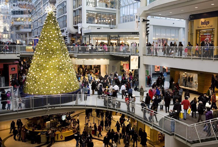 People seen on escalators and walking through a mall next to a large Christmas tree during the holiday season.